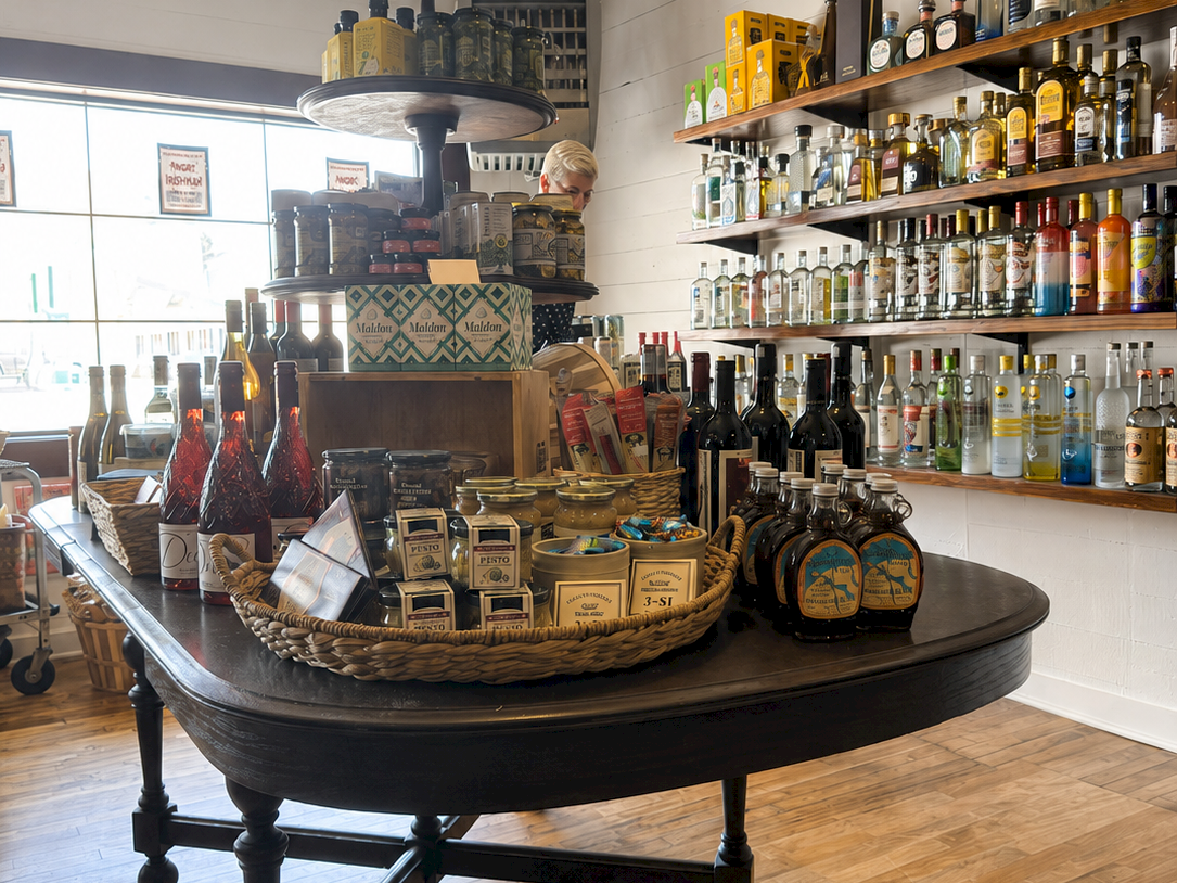 A bar shop display: shelves packed with liquor bottles and a round cart table with spirits, gift boxes, and decanters.